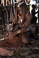 Femme de l'ethnie Himba pilant une pierre rouge (hmatite) - NAMIBIE