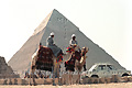 Deux hommes à dos de dromadaire devant les pyramides de Guizeh - EGYPTE